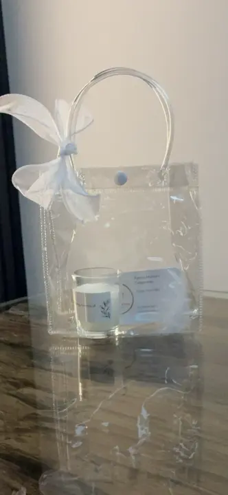 CLAIRE EVANS-BELL: clear gift bag with white ribbon bow holding a labelled glass candle on a wooden surface